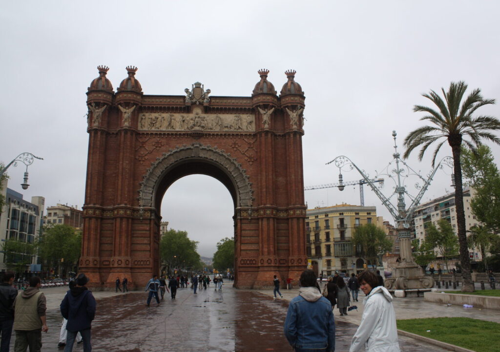 L'Arc de Triomf de Barcelone sous un ciel gris, pavés mouillés et passants en ciré