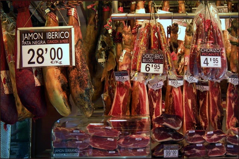 Jambons ibériques et chorizos suspendus avec leurs prix au kilo, sur un étal barcelonais