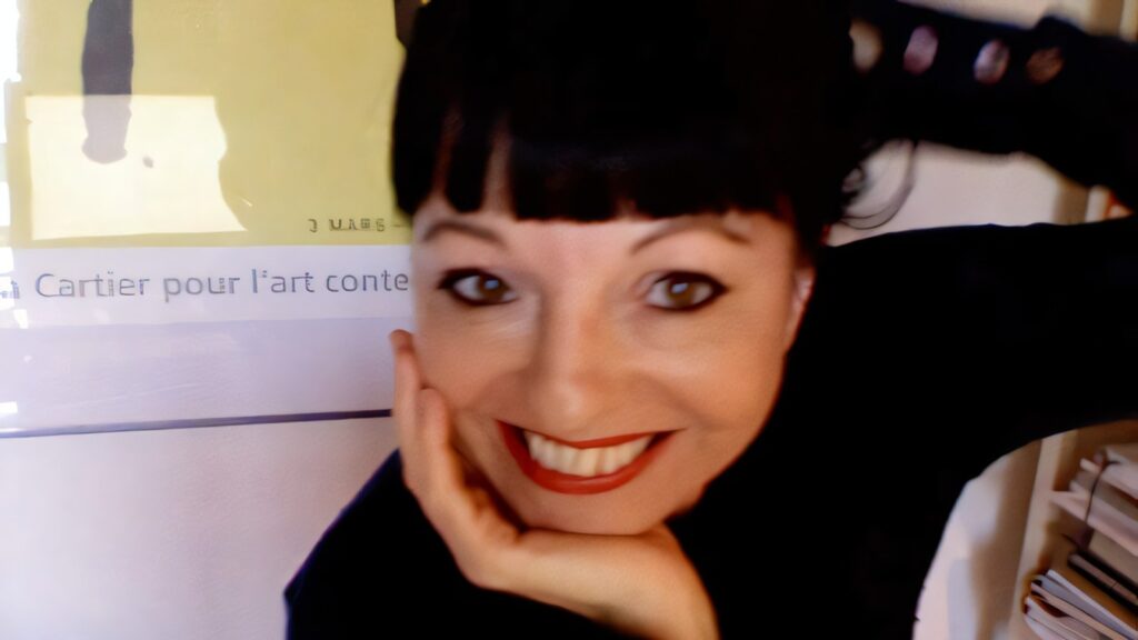 Corinne Bernard, lectrice-correctrice pour l’édition, le menton posé dans la main, souriante, devant une affiche encadrée.
