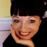 Corinne Bernard, lectrice-correctrice pour l’édition, le menton posé dans la main, souriante, devant une affiche encadrée.