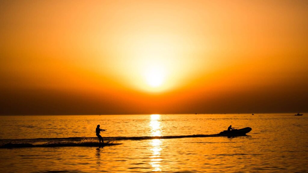 Un skieur nautique tracté par un bateau, en silhouette sur une mer orangée au coucher du soleil, au large de la côte du Maresme.