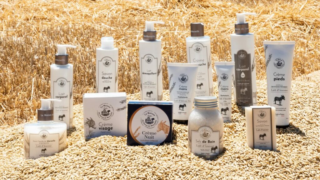 La gamme de La Maison du Savon de Marseille posée sur de la paille : savons, laits corporels, crèmes et sels de bain au lait d’ânesse